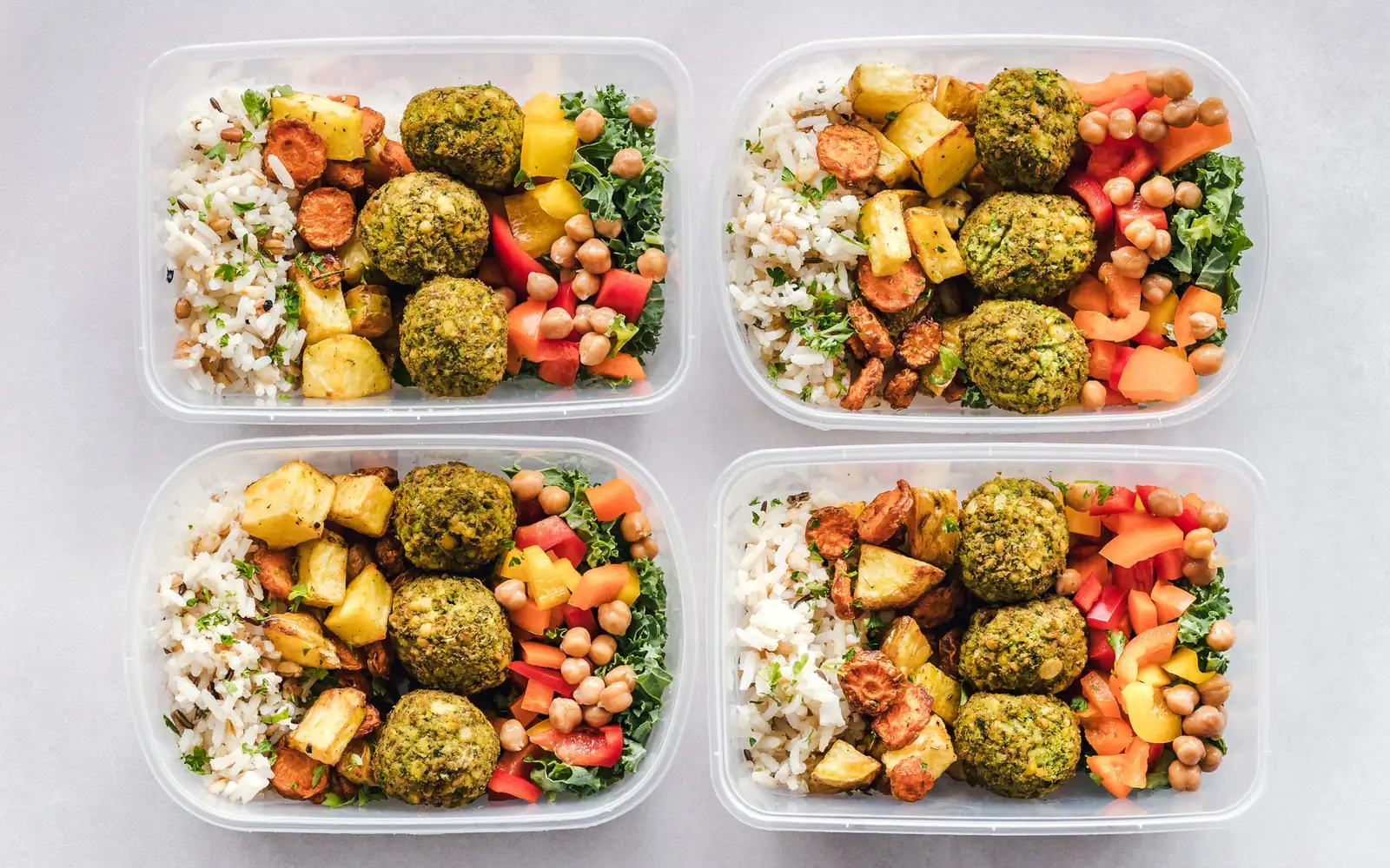 Four meal prep containers with rice, falafel, roasted vegetables and chickpeas, seen from above.