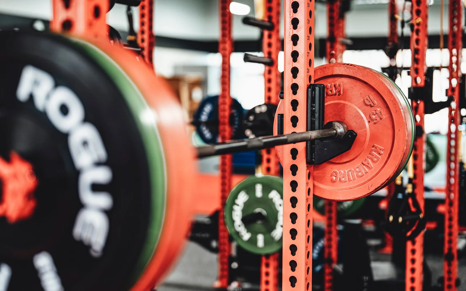 A loaded barbell resting in a red power rack in a gym.